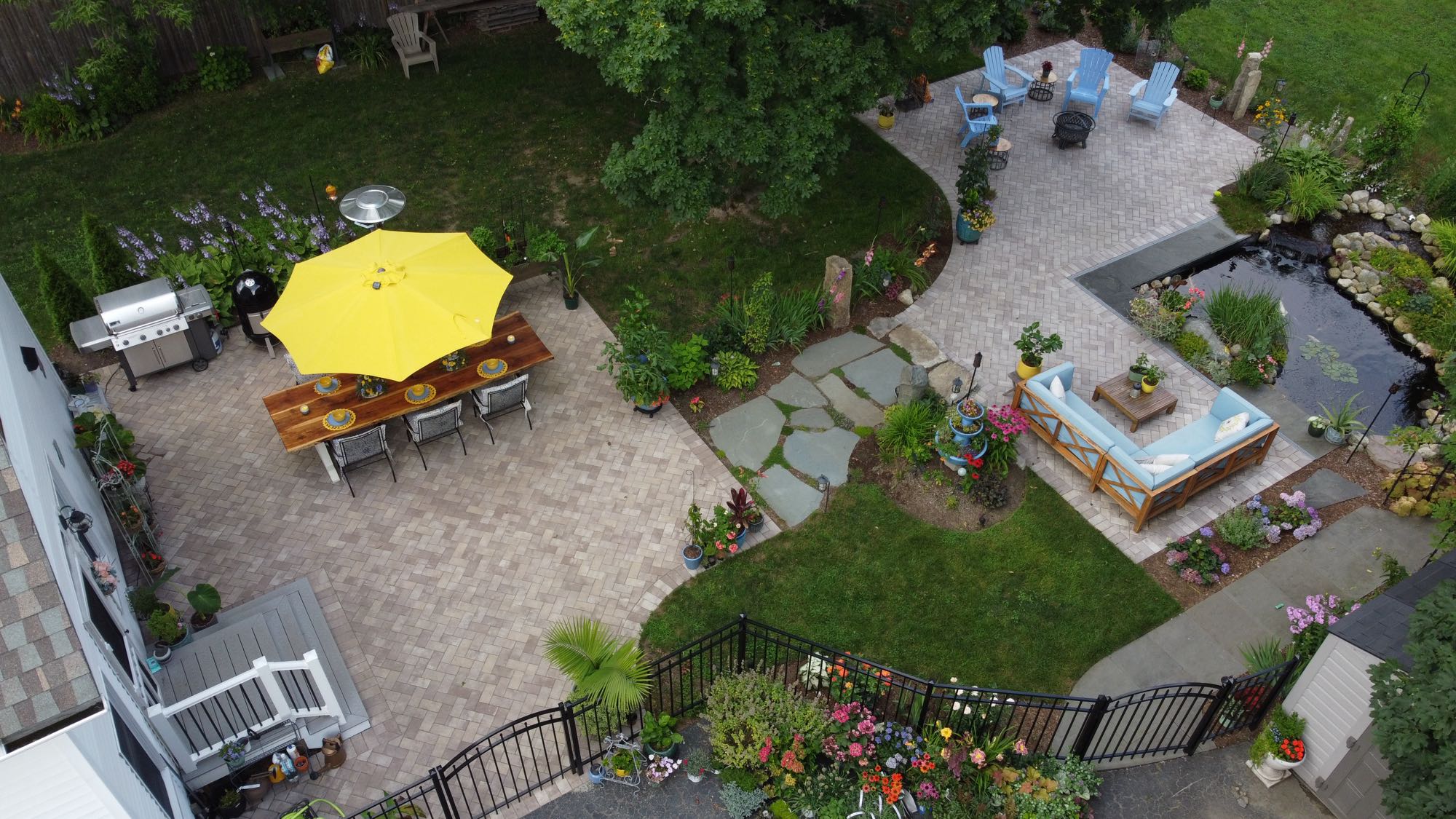 Arnold Ave project; view overlooking two paver patios and natural stone walkway with koi pond, dining set, grill sectional, Adirondack chairs and beautiful landscaping