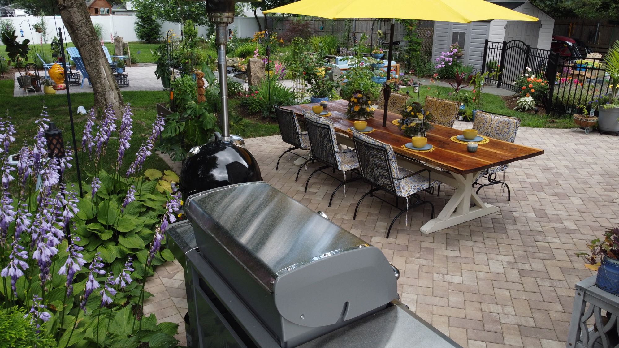 Arnold Ave project; view from behind grill looking over paver patio with dining set and beautiful foliage