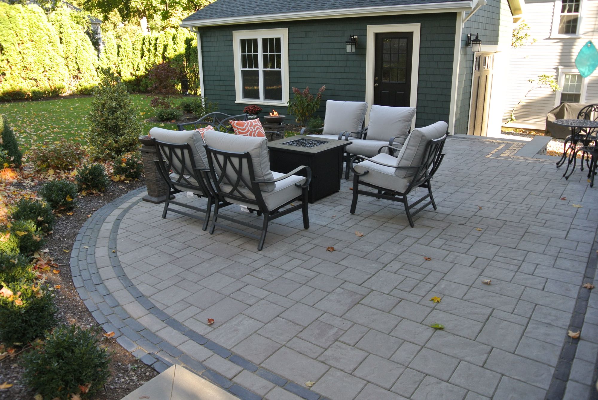 Greene Street project; small paver patio with fire pit and cushioned seating in front of stylish shed/garage