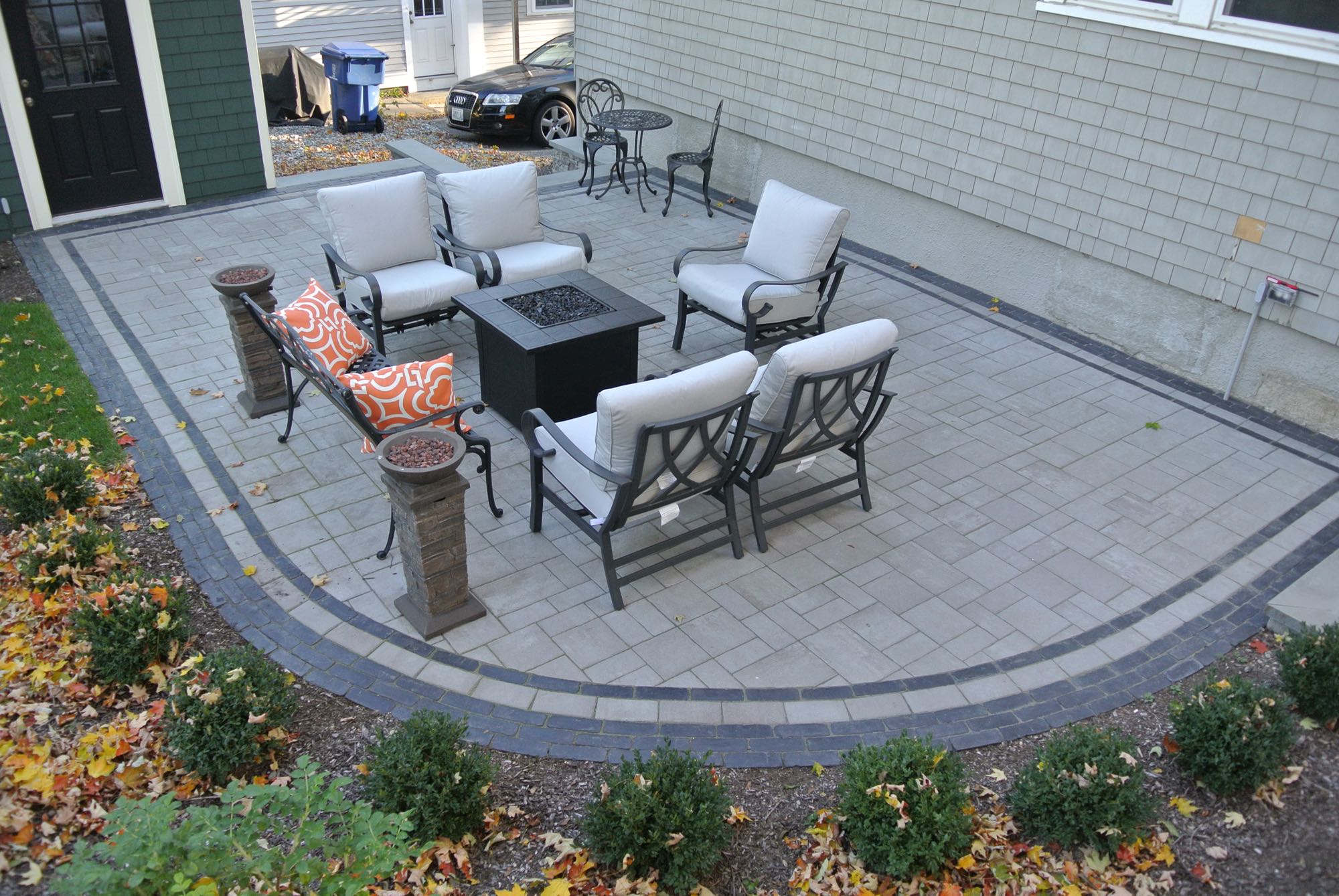 Greene Street project; small paver patio with fire pit and cushioned seating and bistro set with car in background