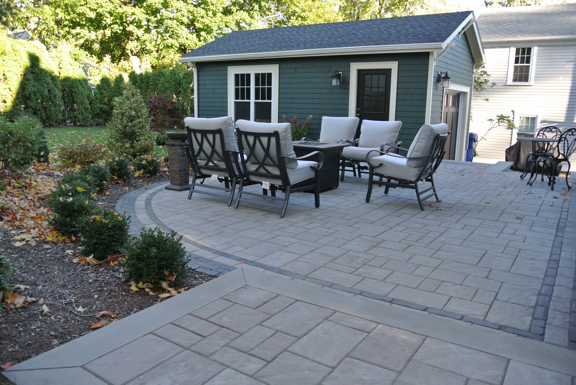 Greene Street project; small paver patio with fire pit and cushioned seating in front of stylish shed/garage