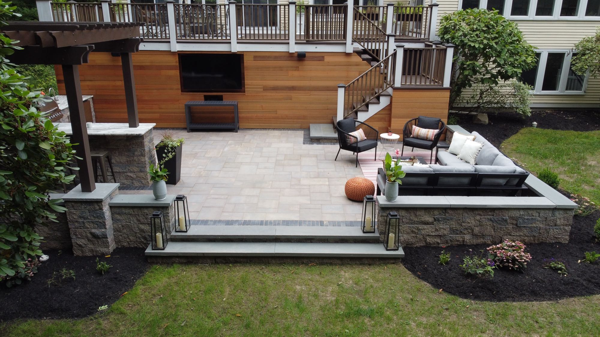 Howland Road project; paver patio entertainment area with stone wall, sectional, and outdoor TV in front of a large wooden deck