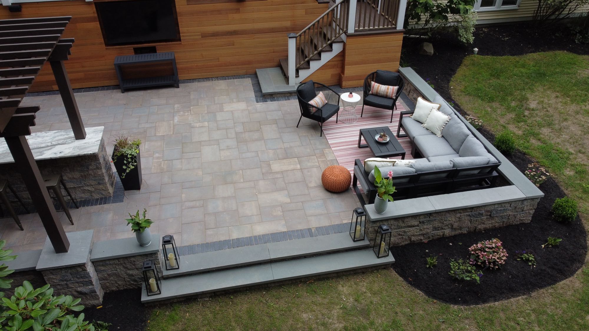 Howland Road project; large wooden deck leading to paver patio entertainment area with stone wall, sectional, and outdoor TV