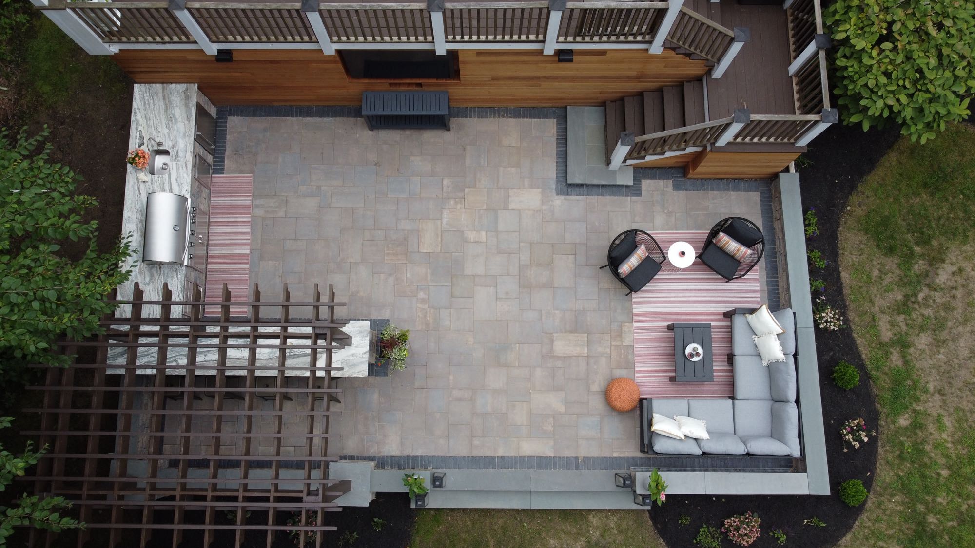 Howland Road project; overhead view of paver patio entertainment area with outdoor kitchen, pergola, outdoor TV and seating area in front of large wooden deck