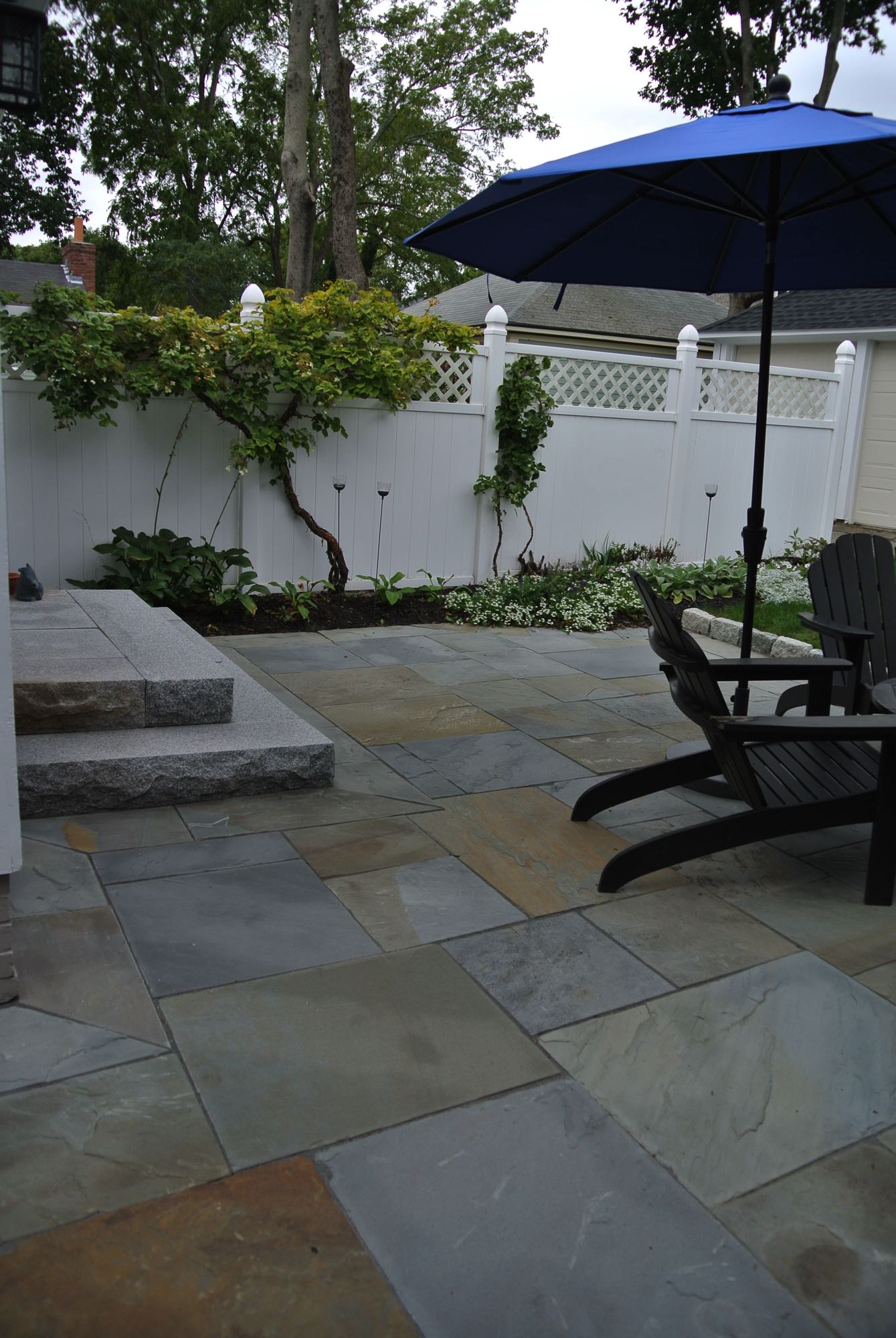 Prospect Street project; natural stone patio with Adirondack chairs and umbrella and stone steps in front of white privacy fence