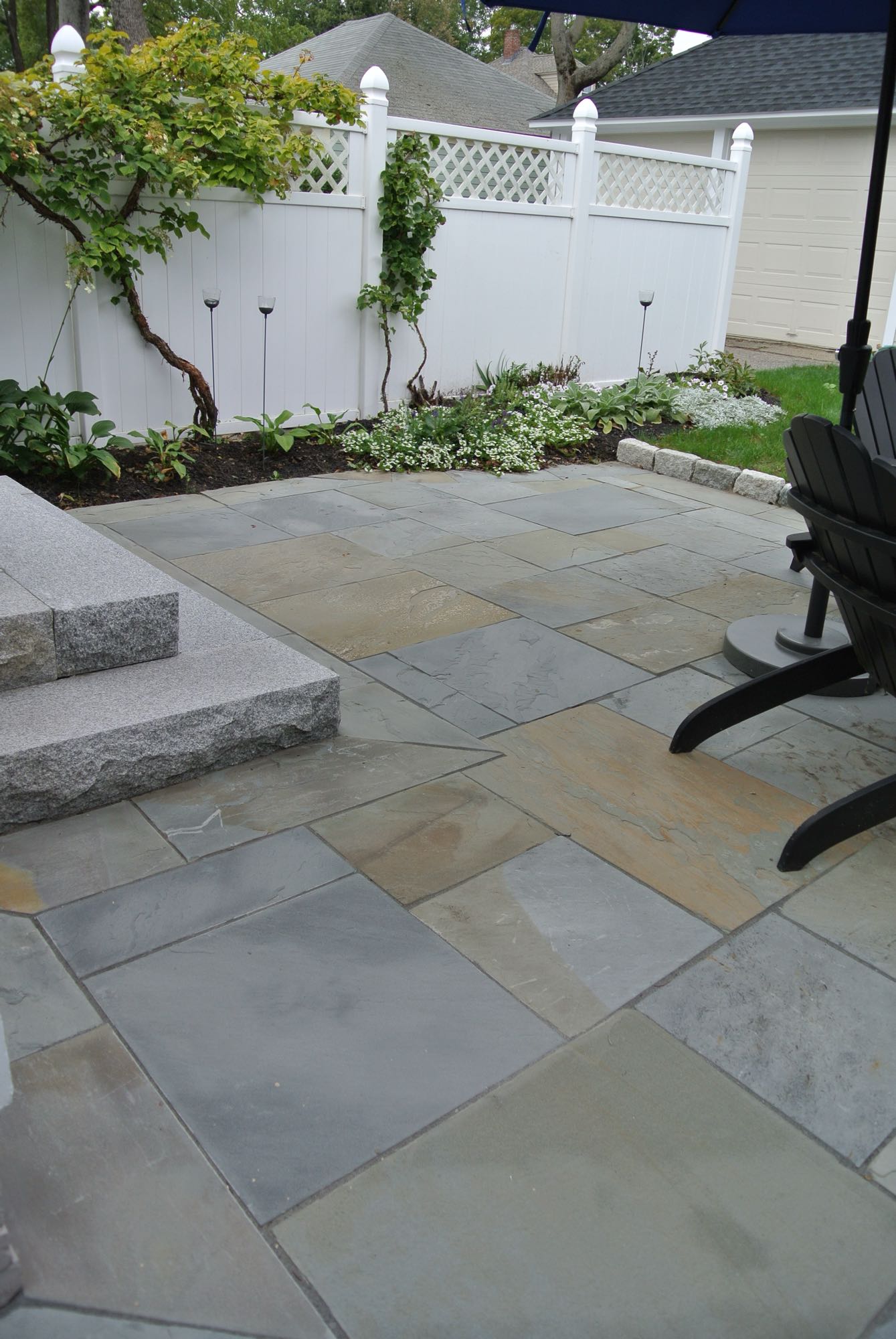 Prospect Street project; natural stone patio with Adirondack chairs and stone steps in front of white privacy fence