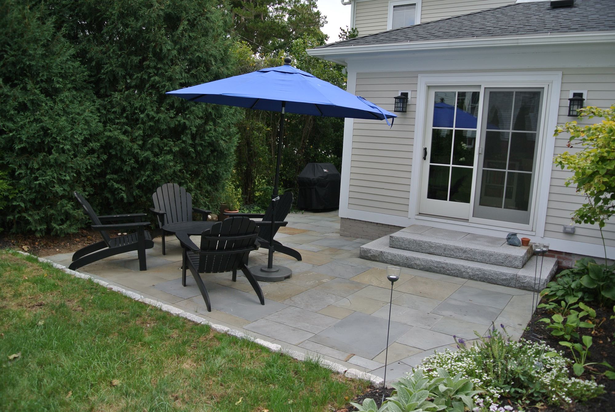 Prospect Street project; small natural stone patio with Adirondack chairs and umbrella and stone steps leading to sliding door into home