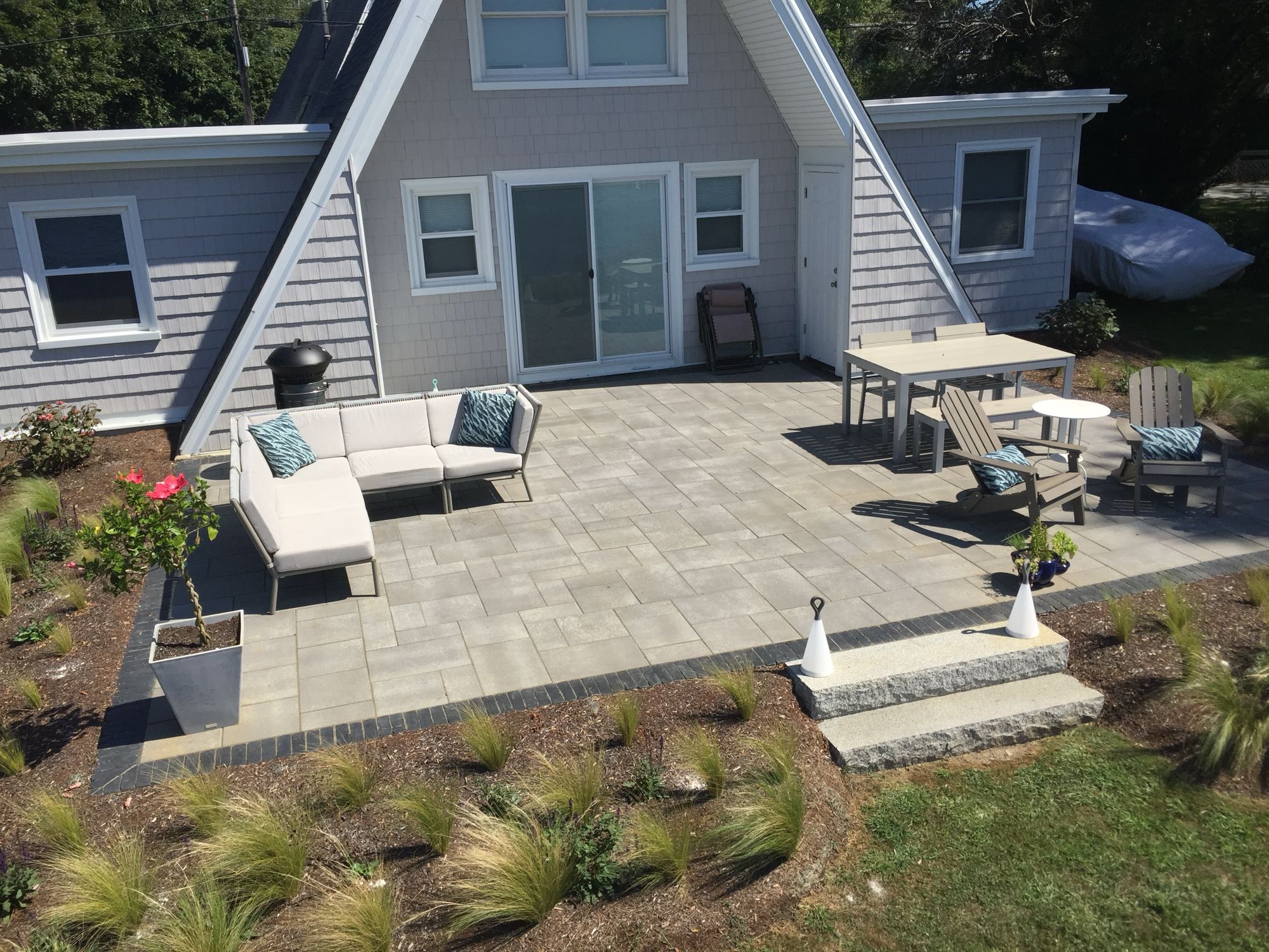 Sapowet patio project; view of A-frame house with small paver patio and natural stone steps with nice patio furniture