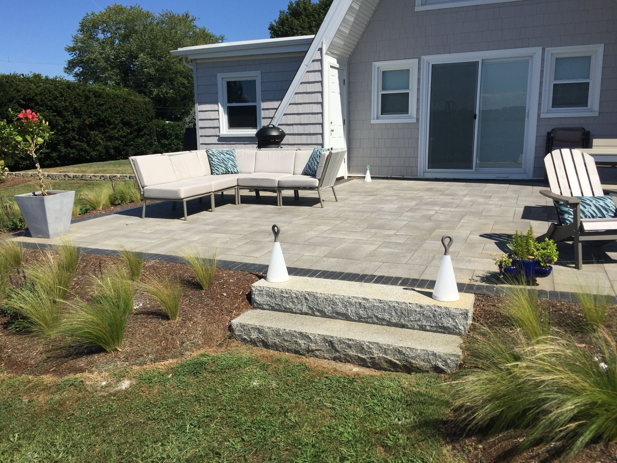 Sapowet patio project; view of A-frame house with small paver patio and natural stone steps with outdoor sectional and an Adirondack chair