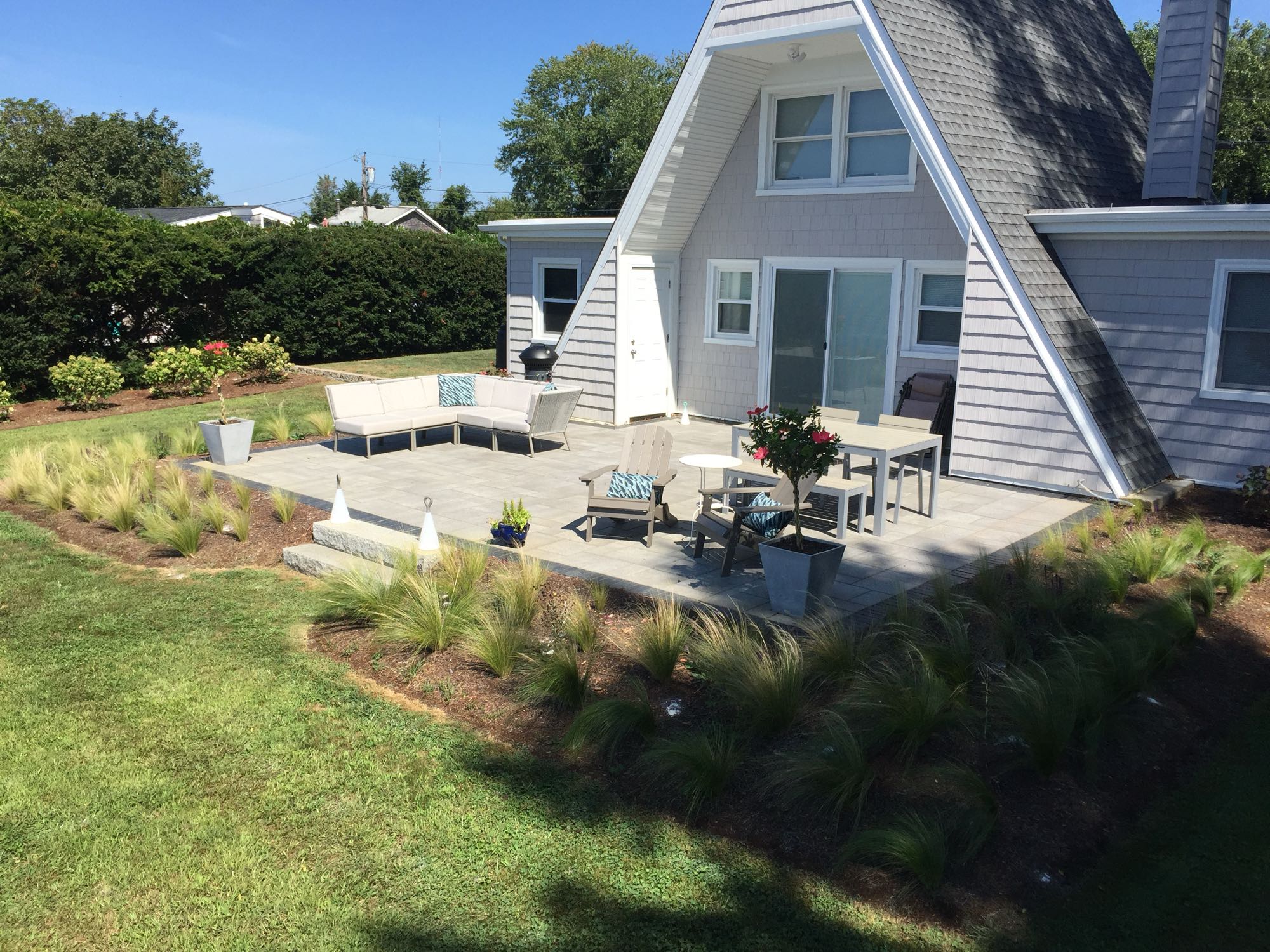 Sapowet patio project; view of A-frame house with small paver patio and natural stone steps with nice patio furniture