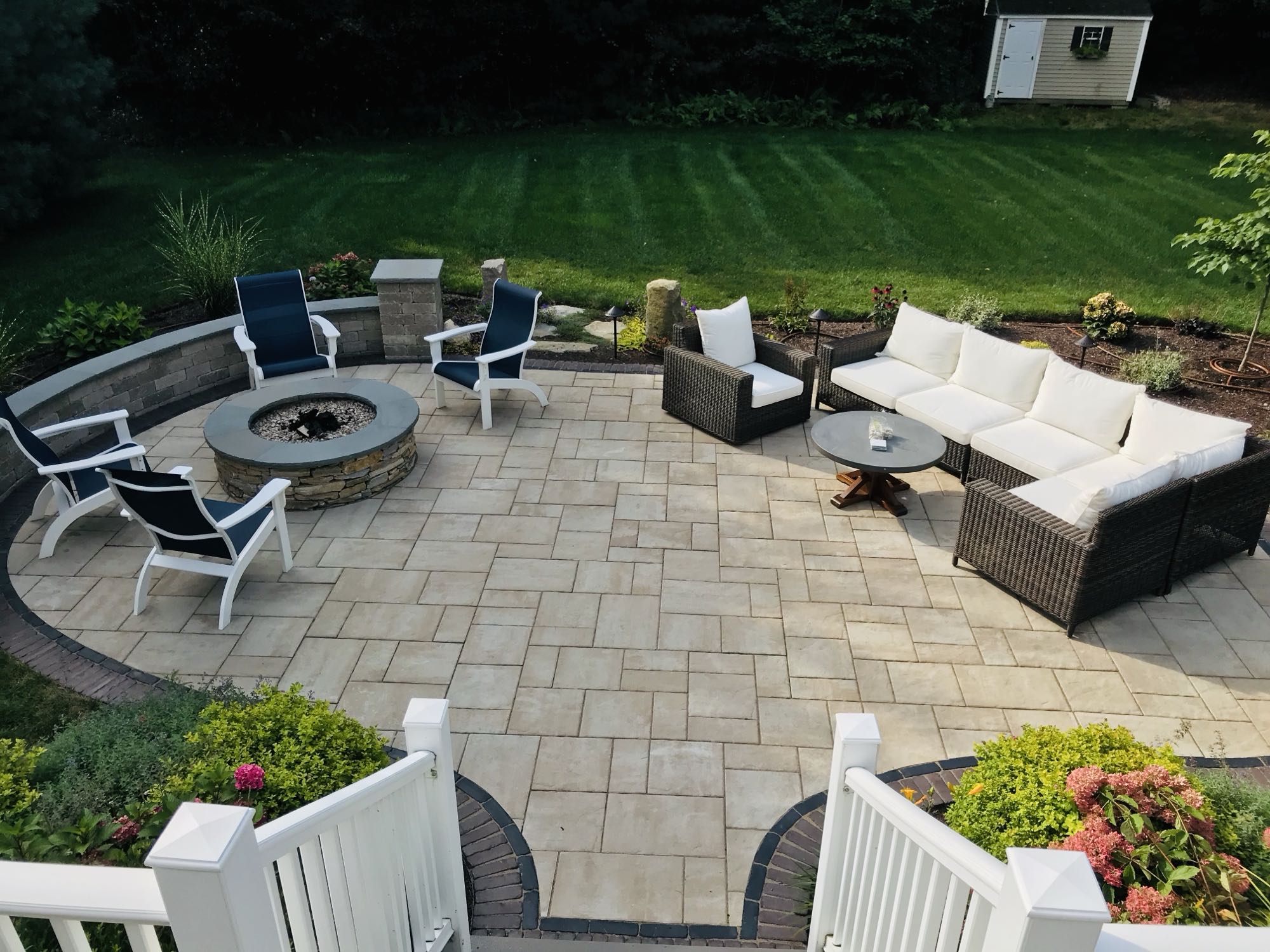 Sylvan Court project; paver patio with short wall around fire pit area and section couch area surrounded by beautiful landscaping