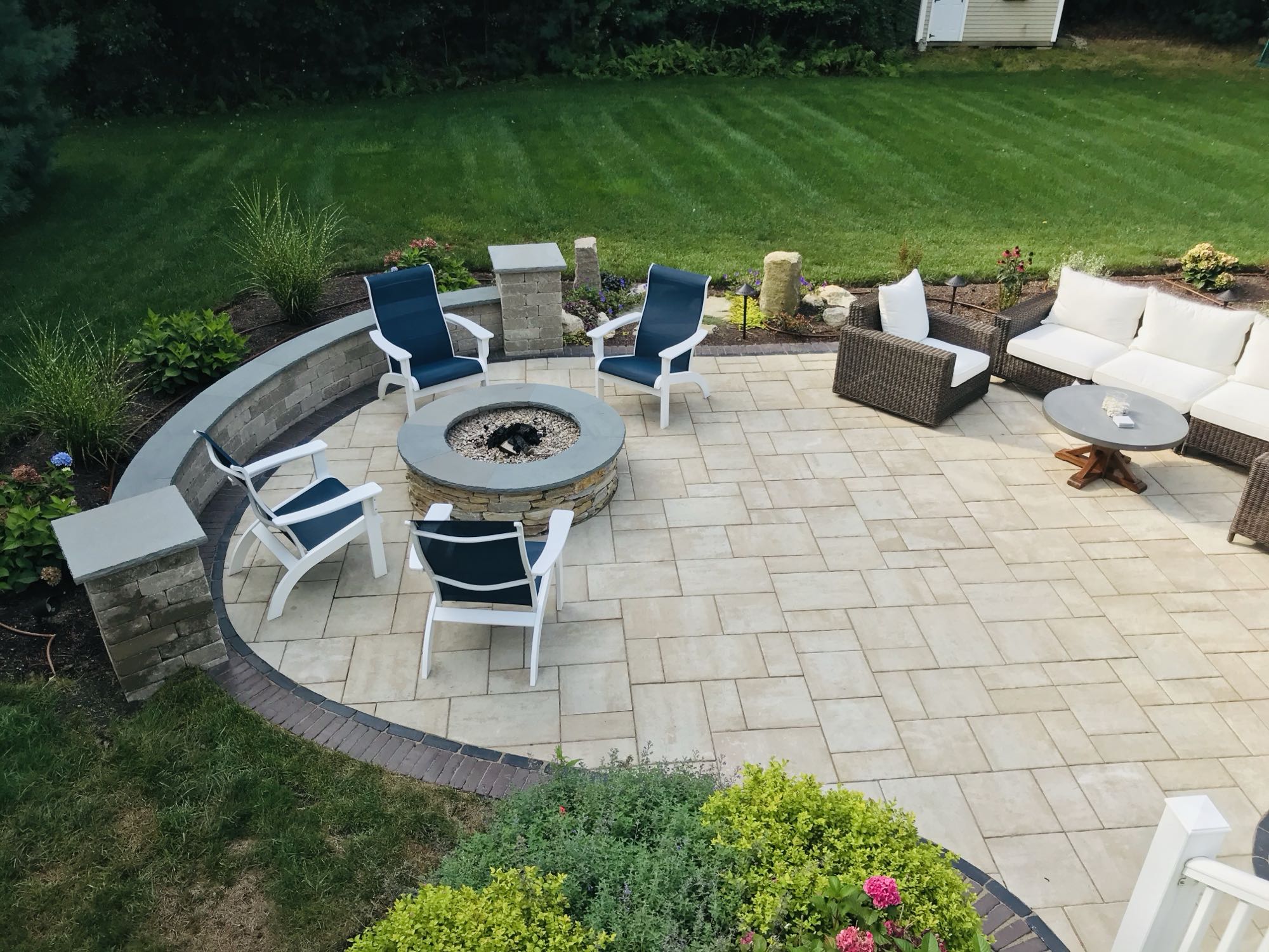 Sylvan Court project; paver patio with short wall around fire pit area and section couch area surrounded by beautiful landscaping