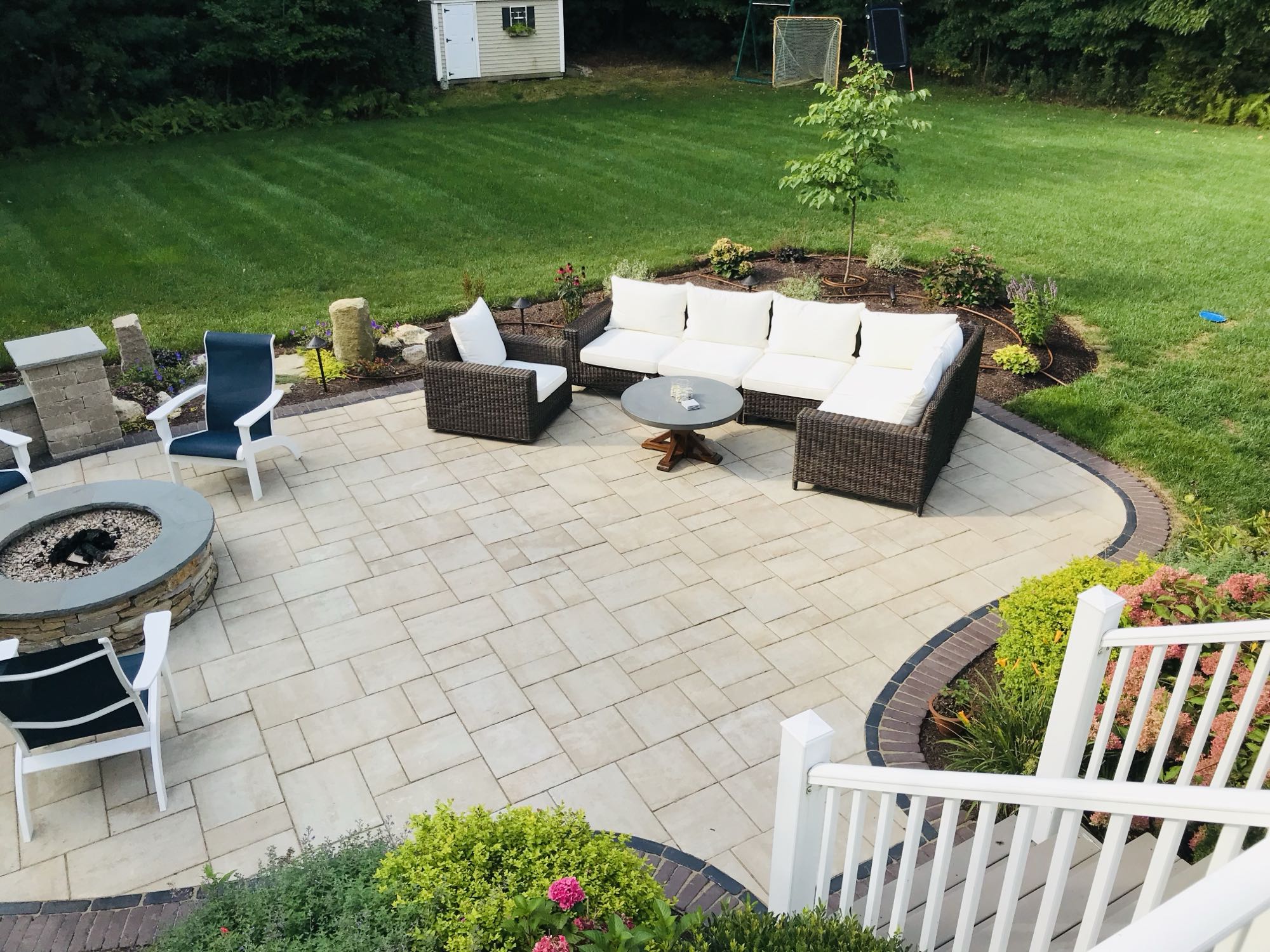 Sylvan Court project; paver patio with short wall around fire pit area and section couch area surrounded by beautiful landscaping