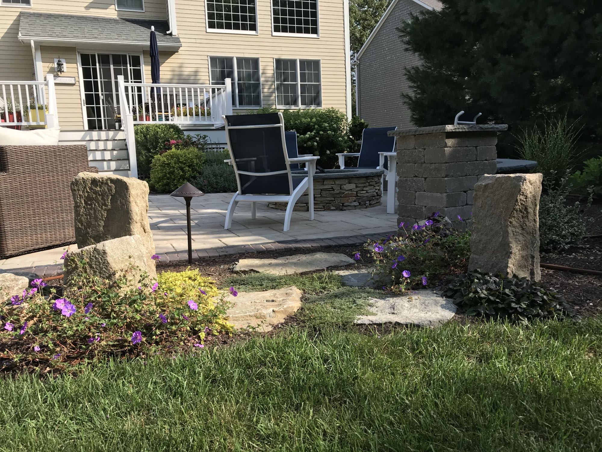 Sylvan Court project; paver patio with with built-in fire pit and natural stone steps through landscaped border to lawn