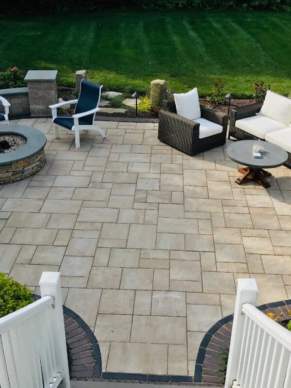 Sylvan Court project; paver patio with short wall around fire pit area and section couch area surrounded by beautiful landscaping