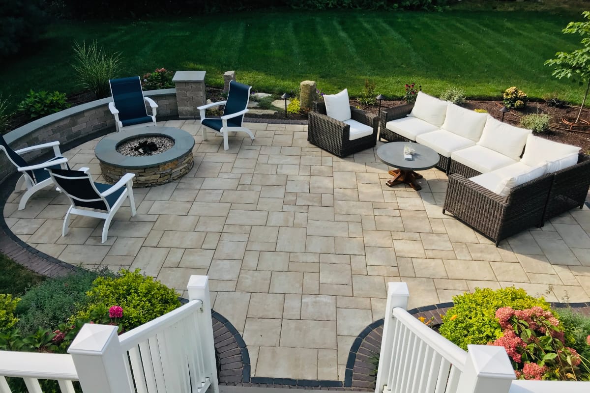 Sylvan Court project; paver patio with short wall around fire pit area and section couch area surrounded by beautiful landscaping