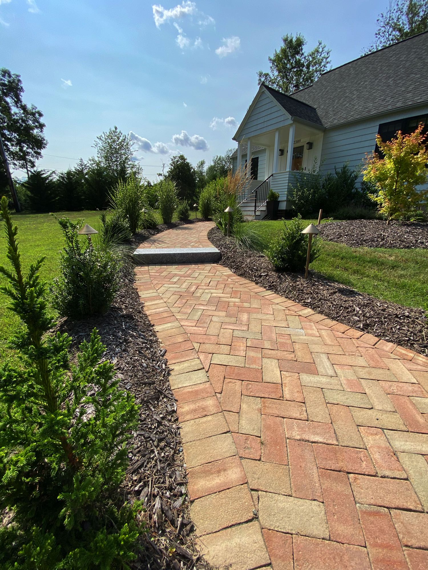 Division Rd project; brick paver walkway in herringbone pattern with stone step bordered by mulch and bushes