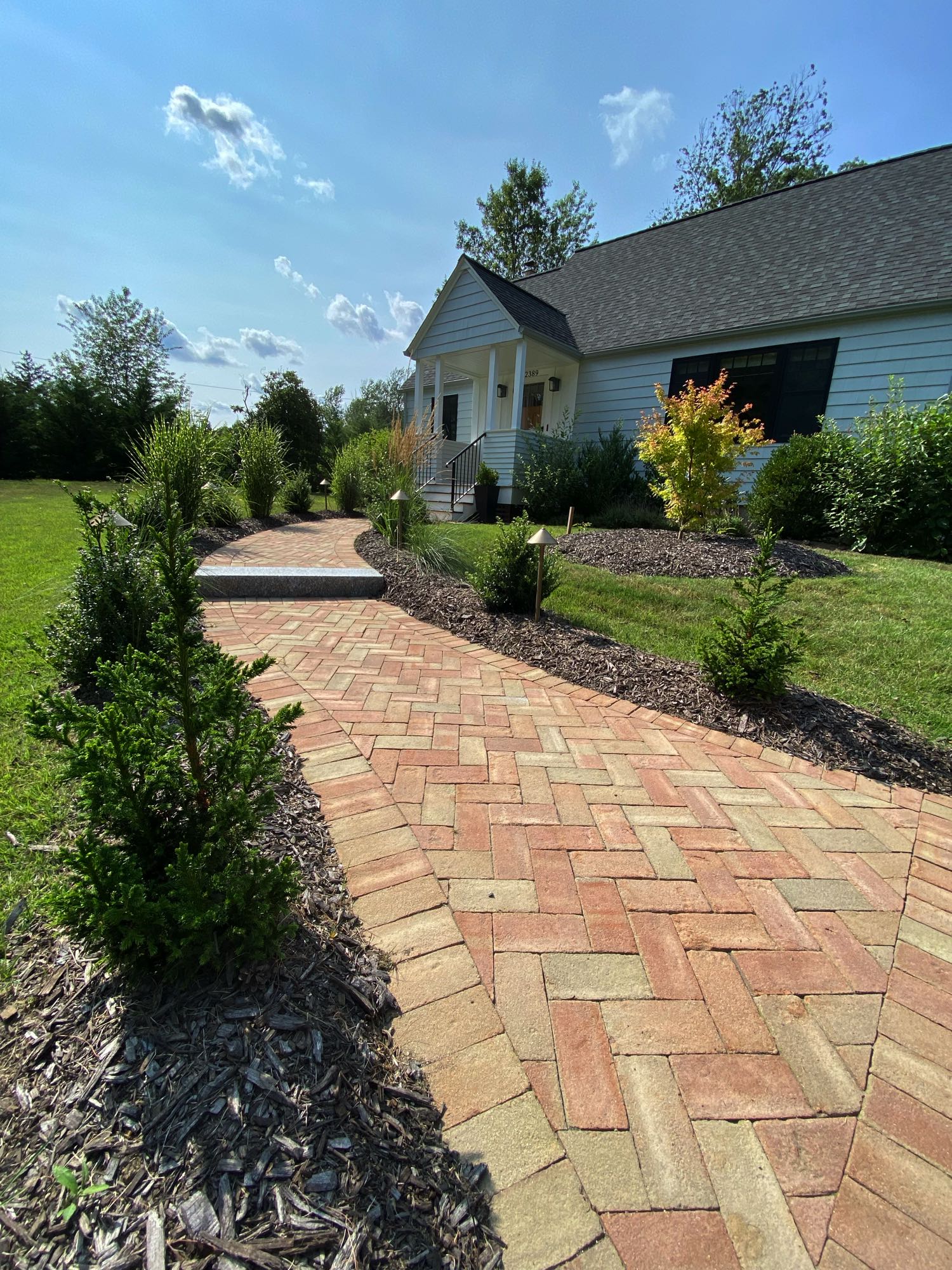 Division Rd project; brick paver walkway in herringbone pattern with stone step bordered by mulch and bushes