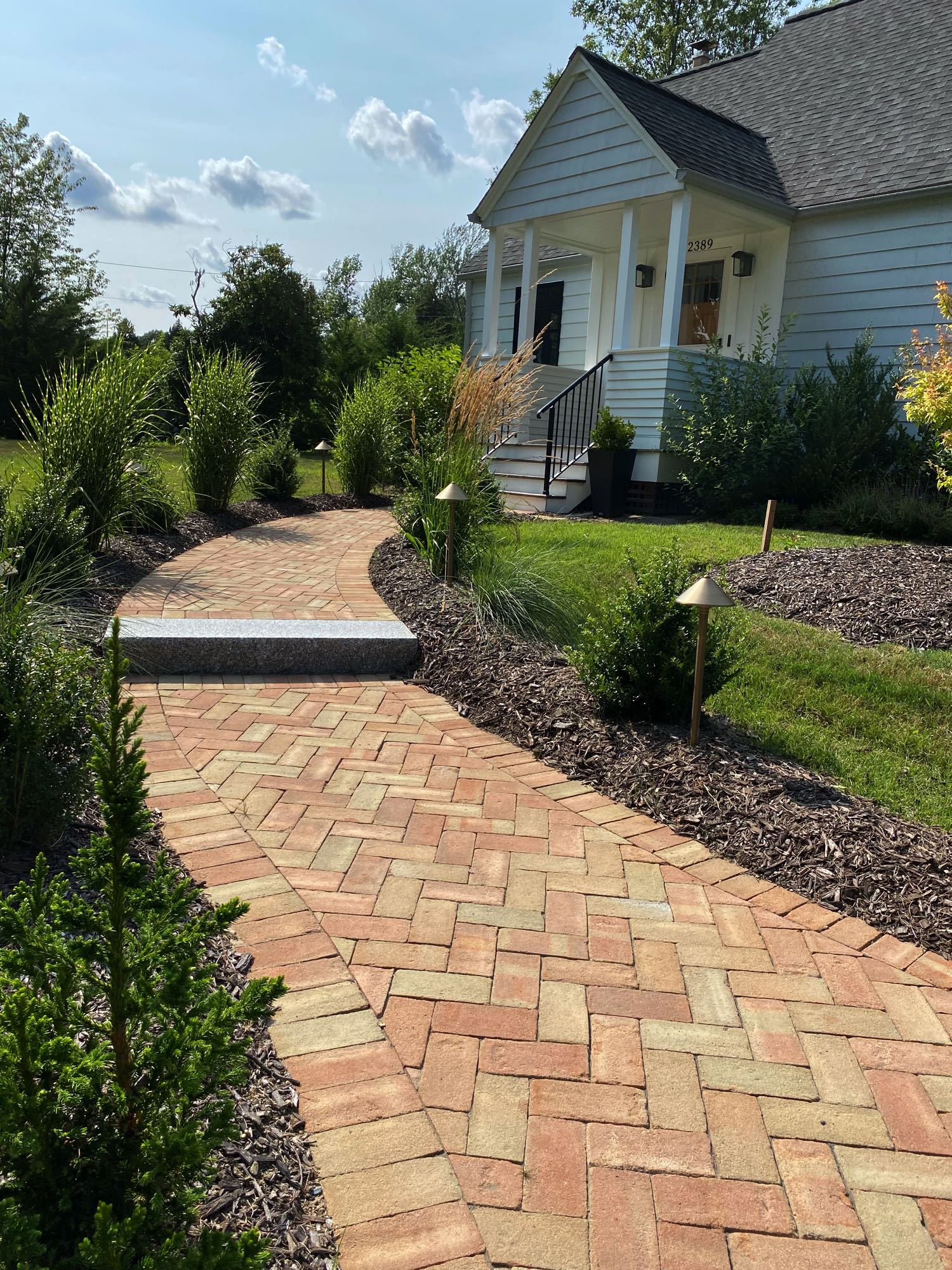 Division Rd project; brick paver walkway in herringbone pattern with stone step bordered by mulch and bushes