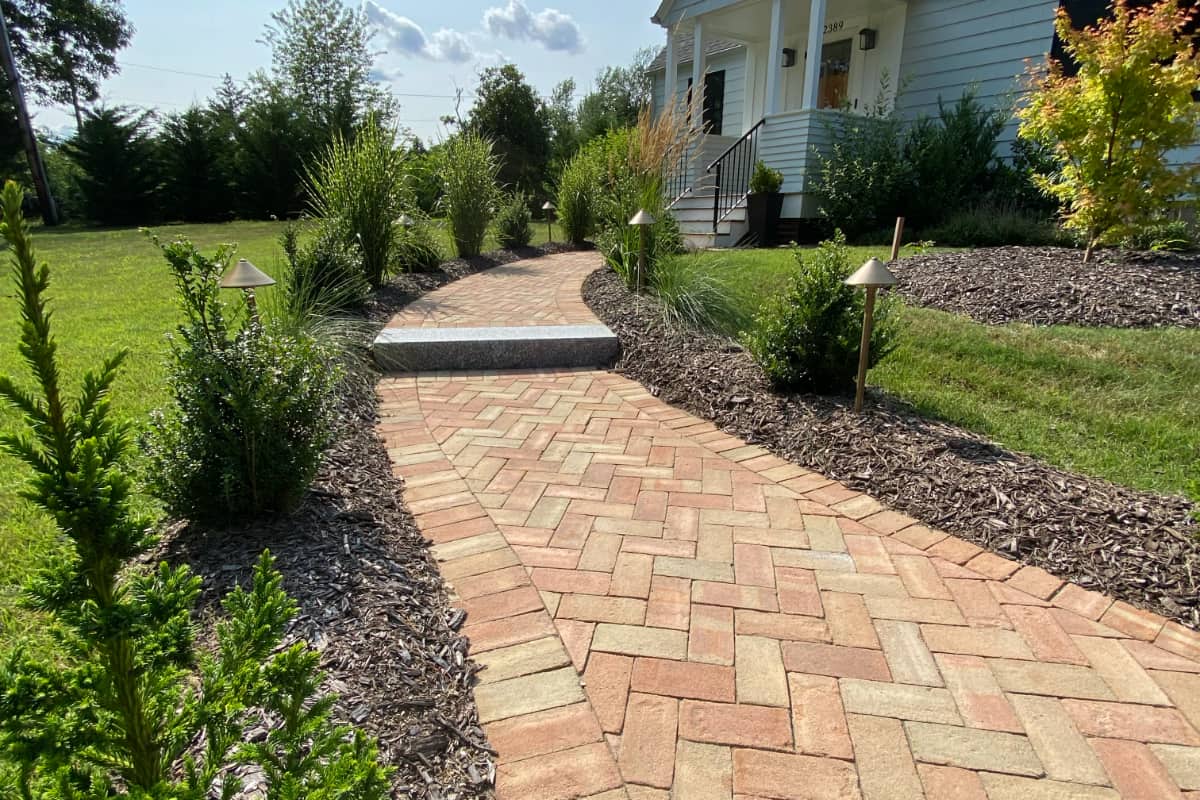 Division Rd project; brick paver walkway in herringbone pattern with stone step bordered by mulch and bushes