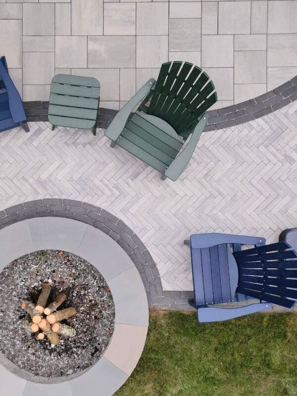 overhead view of a paver stone patio with multiple patterns and a paver fire pit with Adirondack chairs