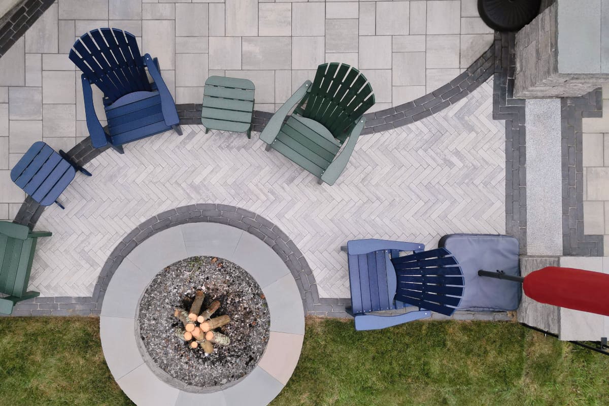 overhead view of a paver stone patio with multiple patterns and a paver fire pit with Adirondack chairs