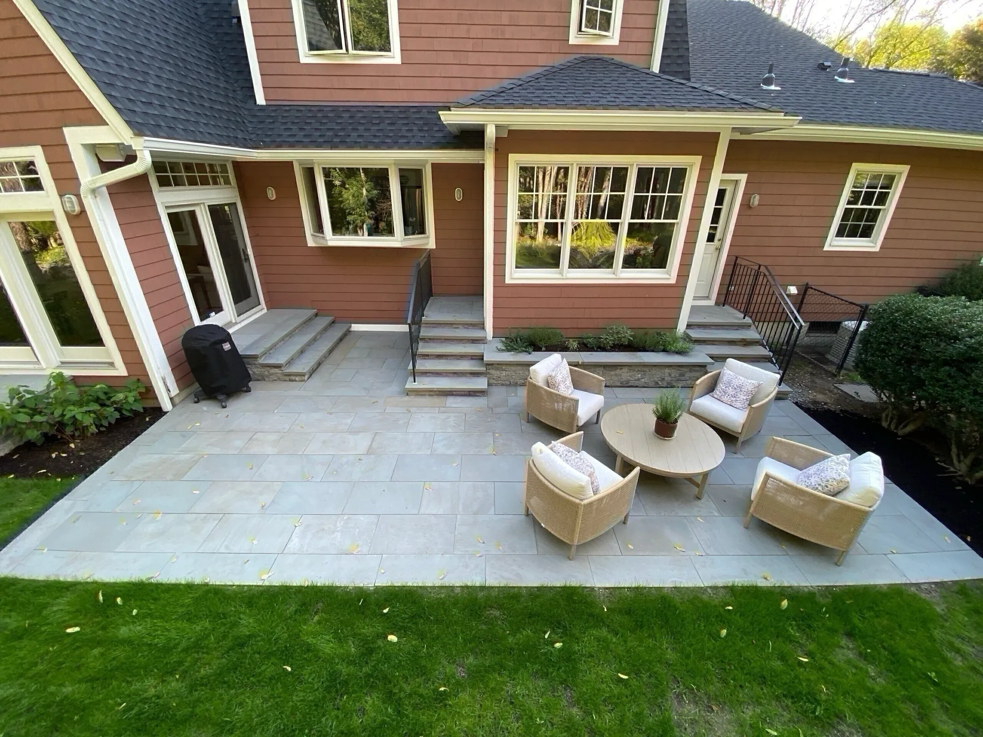 A spacious outdoor patio features light gray stone and multiple stone staircases leading to the brown-sided home, complete with wicker seating.