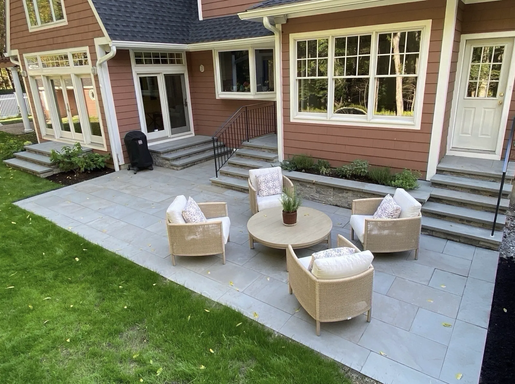 A gray stone patio with a wicker outdoor furniture set. The patio connects to the house via several custom stone staircases.